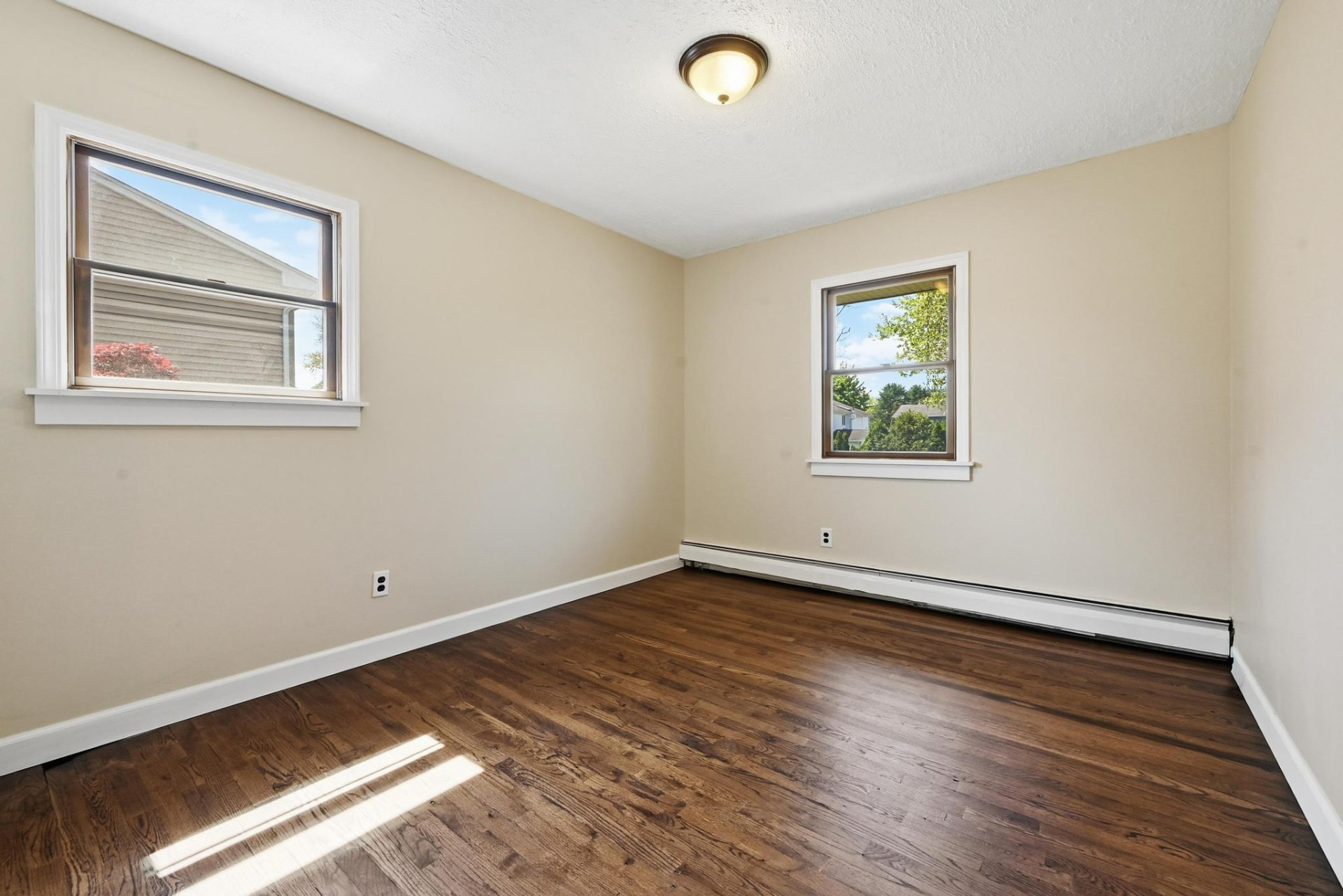 The same secondary bedroom after the work, emptied with refinished hardwood floors and freshly painted walls
